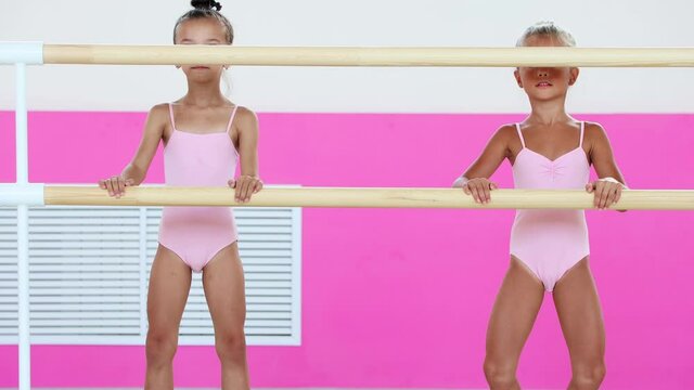 Two little girls gymnasts warming up in the studio leaning on a handrail