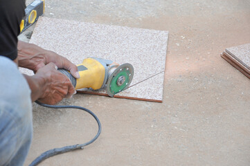 a worker cutting a tile by using an angle grinder on the floor at construction site