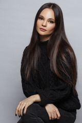 Stylish portrait of a beautiful brunette girl in a black sweater isolated on a gray background.