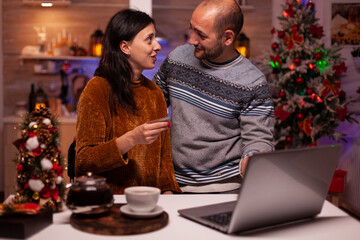 Joyful family doing online shopping using credit card paying xmas gift present on laptop celebrating winter season. Happy romantic couple celebrating christmas holiday in x-mas decorated kitchen