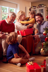 Multi-Generation Family Exchanging And Opening Gifts Around Christmas Tree At Home