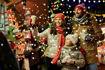 family, winter holidays and celebration concept - happy mother, father and little daughter with takeaway drinks at christmas market on town hall square in tallinn, estonia over snow