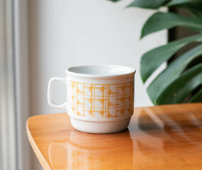 Mid-century modern porcelain cup with yellow pattern on a wooden table with philodondendron in the background