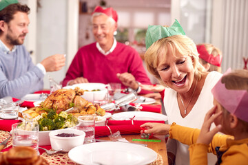 Multi Generation Family In Santa Hats Enjoying Eating Christmas Meal At Home Together