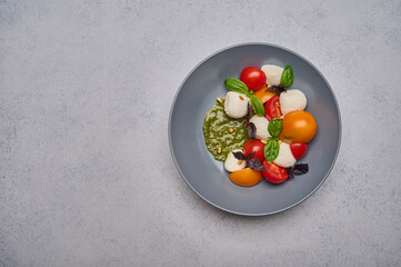 Italian caprese salad with ripe tomatoes, pesto, basil and mozzarella cheese in grey deep plate. Top view, copy space