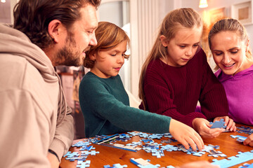 Family Sitting Around Table At Home Doing Jigsaw Puzzle Together