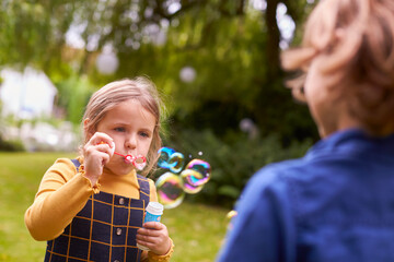 Obraz premium Boy And Girl Having Fun In Garden Blowing Bubbles Together