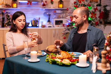 Cheerful romantic couple eating christmas dinner sitting at dinning table in xmas decorated kitchen. Haapy family enjoying christmastime celebrating winter holiday together