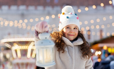 winter holidays and children concept - portrait of happy little girl with lantern over christmas...