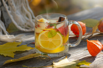 Autumn still life with a cup of fruit, books, a warm handkerchief, and fallen leaves around.