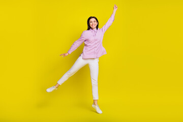 Full size photo of funny brown hairdo young lady jump arm up wear pink shirt pants isolated on yellow color background