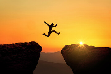 Man jumps from cliff to cliff over a precipice at sunset, a creative idea. Success and Risk Concept