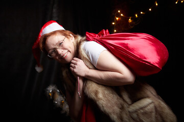 A cheerful dwarf with big red bag at home. Assistant of Santa Claus in a red hat and with glowing...