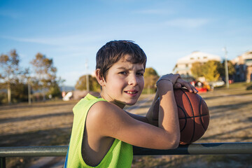 Young teen male with sleeveless standing on a street basket court while smiling at camera