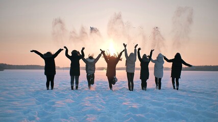 A group of girls friends are throwing snow up at sunset.