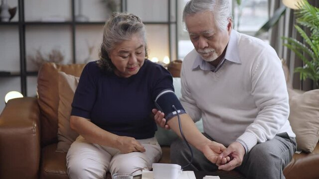 Asian elderly couple using a blood pressure monitor to the wife in the house