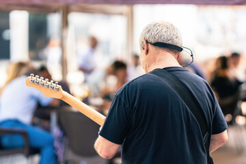 Back of an elder man playing the electric guitar on a live concert in the terrace
