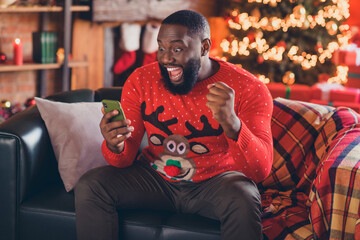 Photo of young excited black man happy positive smile rejoice celebrate victory smartphone noel xmas winter indoors