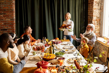 Happy Thanksgiving dinner party with family and friends with turkey and holiday traditional food, dishes on table.