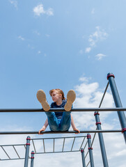 Young girl climbs the bar on the playground. Child sports concept. Healthy lifestyle.