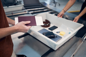 Passenger holding passport against personal Items, liquids, and laptop in container at airport...