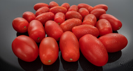 Plum tomatoes and cherry tomato composition on a dark glass background. Vegan food