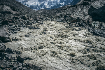 Scenic highlands landscape of powerful mountain river beginning from glacier among large moraines. Beautiful scenery with glacier at source of turbulent river. Mountain river source among big stones.