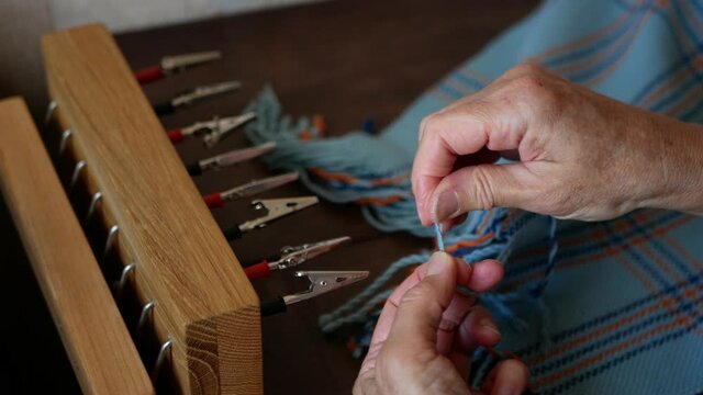 Woman is creating a fringe on a handmade scarf or shawl using special tool. Artisan is in action. Hands of artisan with woven product