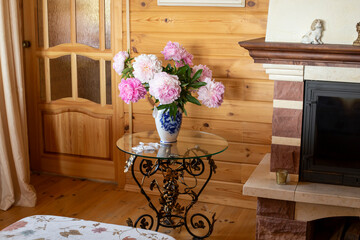 A beautiful wrought-iron table with a vase of flowers in the living room near the fireplace. Cozy interior of a country house