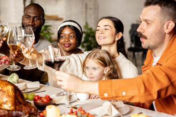 Close-up happy multiethnic big family celebrate Thanksgiving day, sitting at table with roasted turkey and holiday traditional food, dishes.