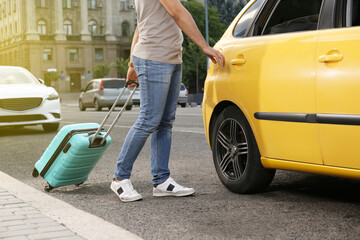 Man with suitcase getting into taxi on city street