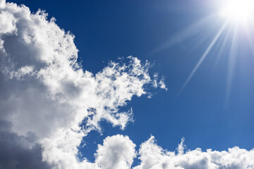 Beautiful blue sky with white cumulus clouds and sun rays. Backlight photography.
