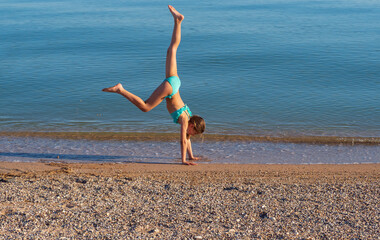A young woman makes a wheel on the street. acrobatic gymnastics girl in a bikini on the beach. A...
