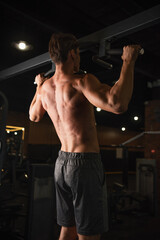 Fototapeta na wymiar back view of shirtless athletic man training on horizontal bar in sports center.
