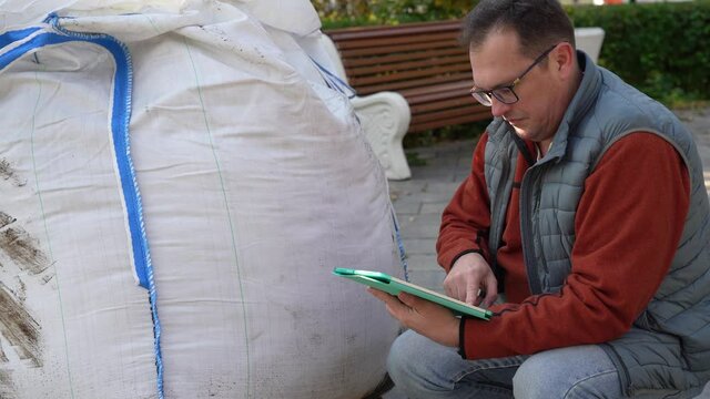 Man with a tablet checks the quality of the contents of a large white bag