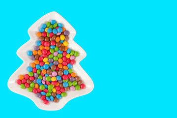 Multicolored round candies in a plate on blue background top view