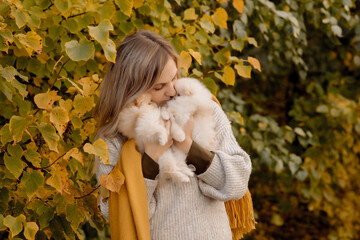 A young blonde woman holds pomeranian puppies in her arms on a walk in the autumn park
