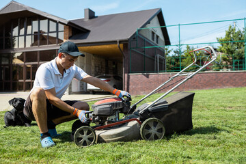 The gardener prepares the lawn mower to start the engine - obrazy, fototapety, plakaty