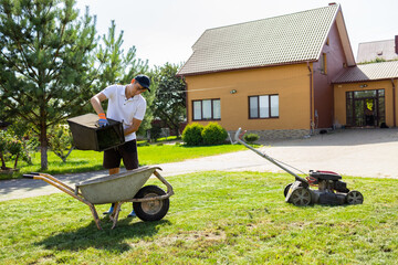 Man unloads mowed grass from a lawn's mower catcher into a wheelbarrow