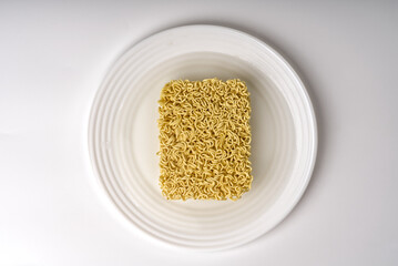 Instant noodles are lying in a white plate on a white background already filled with hot water.