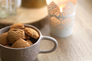 Bowl of cinnamon cookies, lit candles and vase with gypsophila flowers on the table. Selective focus, fairy lights in the background. Hygge at home.