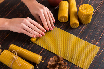 Women's hands make handmade candles of natural wax with texture of honeycomb bees, on a wooden...