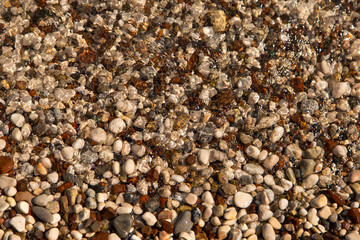 The beach is made of pebbles, the seashore, small colored pebbles in the water. Background, copy space.