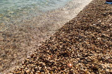 The beach is made of pebbles, the seashore, small colored pebbles in the water. Background, copy space.