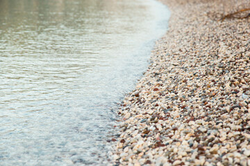 The beach is made of pebbles, the seashore, small colored pebbles in the water. Background, copy space.