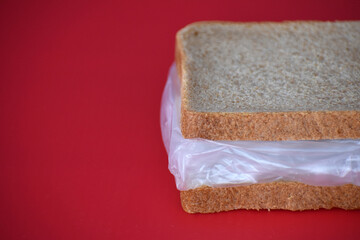 Sandwich with bread and plastic on a red background. Harmful for the food chain.