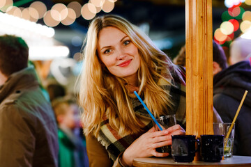 Happy young woman drinking hot punch, mulled wine on German Christmas market. Happy person in...