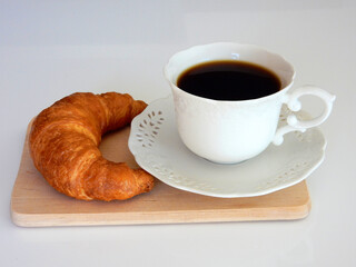 Coffee in a white cup and croissant on the table for breakfast