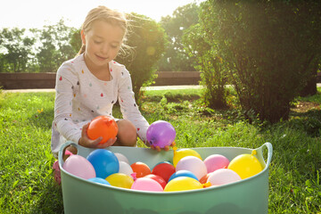 Little girl with basin of water bombs in park on sunny day