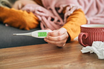 Unrecognizable ill woman holding thermometer showing her temperature